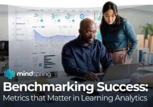 A young asian female standing behind a middle aged African American male who's at his desk looking at a laptop with a holographic metrics dashboard in the background reviewing learning analytics, with the title of the article overlayed on top